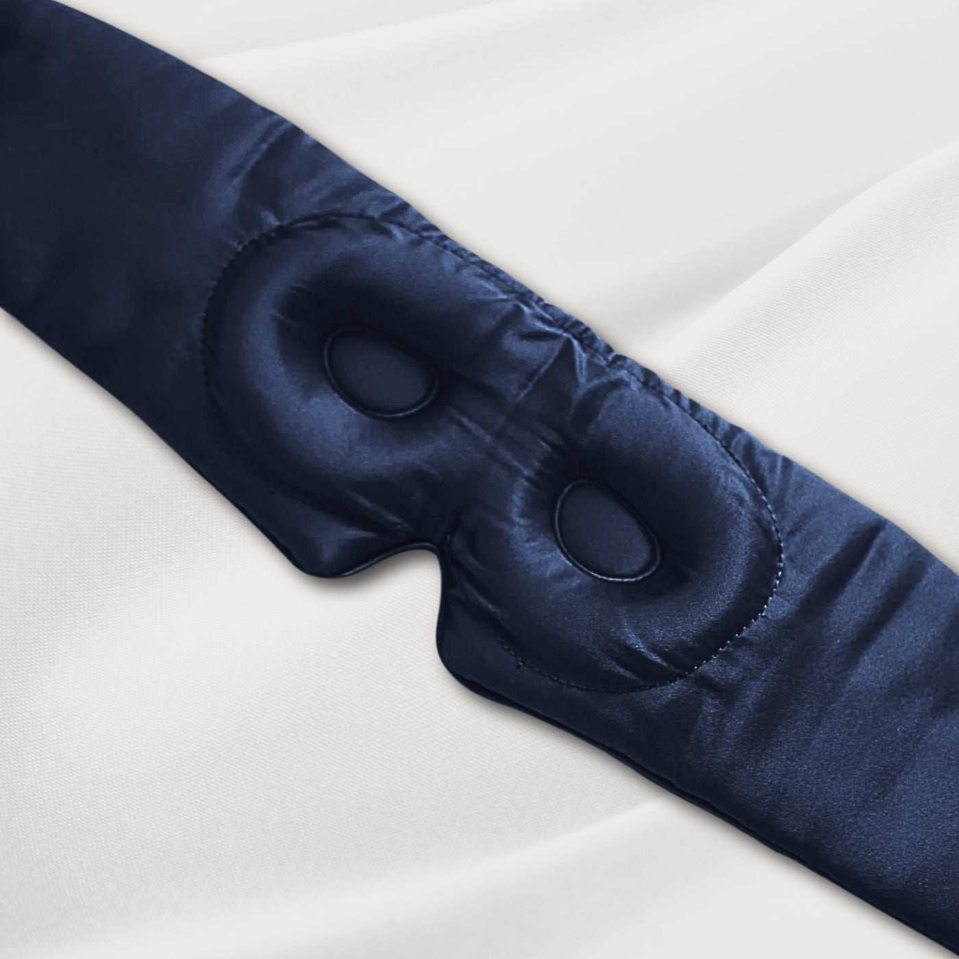 Blue LashGuard 3D sleep mask resting on white bedding, angled view of the contoured eye cups