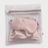 A mesh laundry bag holding a pink silk sleep mask, zipped shut