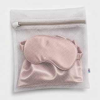 A mesh laundry bag holding a pink silk sleep mask, zipped shut